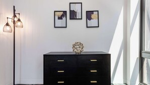 A black dresser with gold handles, a geometric vase, and three framed abstract paintings on a white wall. - Downtown Chicago Stay with Free In & Out Parking-2 (Chicago)