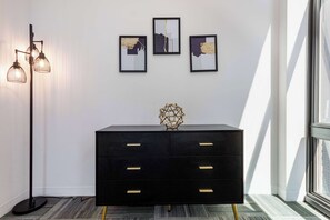 Een zwarte dressoir met gouden handgrepen, een geometrische vaas en drie abstracte schilderijen in lijsten op een witte muur.