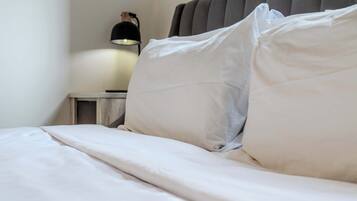 A neatly made bed with white linens, a bedside lamp, and a gray upholstered headboard.