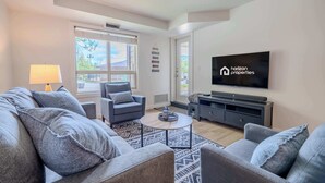 Una sala de estar moderna con sofá, sillones, una mesa de centro, televisor y un ventanal grande.