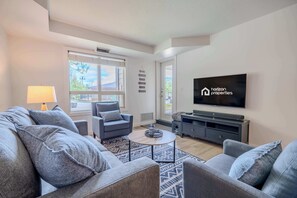 Een moderne woonkamer met een bank, fauteuils, een salontafel, een televisie en een groot raam.