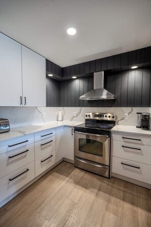 Een moderne keuken met witte kastjes, een roestvrijstalen fornuis en een zwarte afzuigkap.