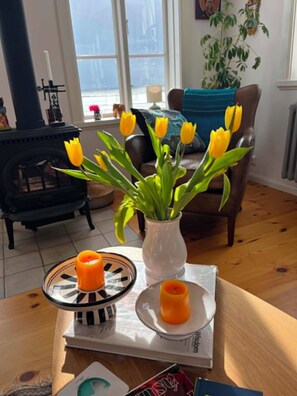 A cozy living room with a fireplace, a vase of yellow tulips, and two candles on a table.