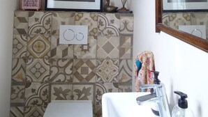 Un baño con pared de azulejos, un cuadro enmarco, un espejo, un lavamanos con grifo y un dispensador de jabón.