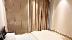 Un dormitorio con cama, ropa de cama blanca, un armario y una cortina.