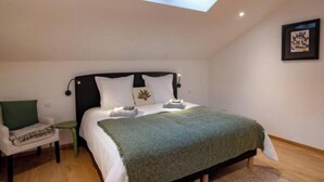 A bedroom with a skylight, a bed with a green blanket, a bedside table, and a chair.