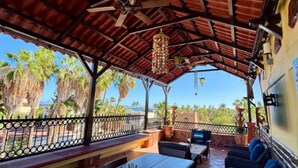 Una terrazza all'aperto con tavoli e sedie in legno, un lampadario e vista su palme.