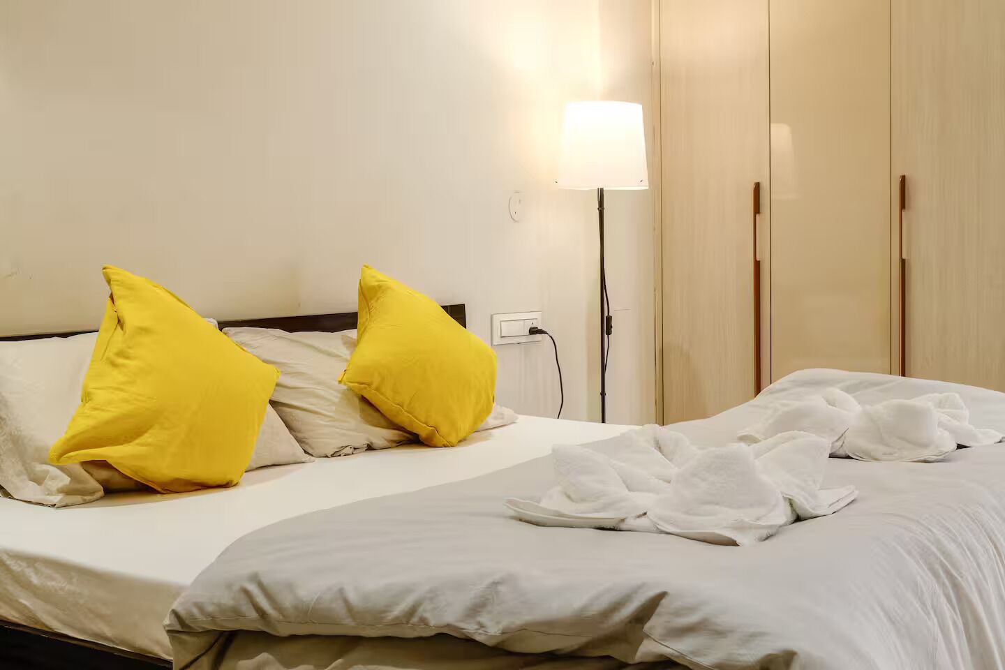 Ein Hotelzimmer mit einem Bett, zwei gelben Kissen, einer Nachttischlampe und einem Kleiderschrank.