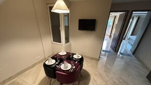 En matplats med ett bord för fyra personer, en tv som är monterad på väggen och en hall som leder till andra rum.