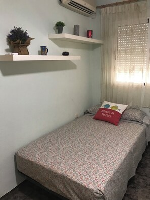 Ein kleines Schlafzimmer mit einem Einzelbett, einer Ablage mit Dekoration und einem Fenster mit Jalousien.