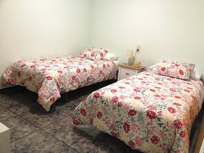 Una habitación con dos camas individuales, una mesita de noche con lámpara y suelo de baldosas.
