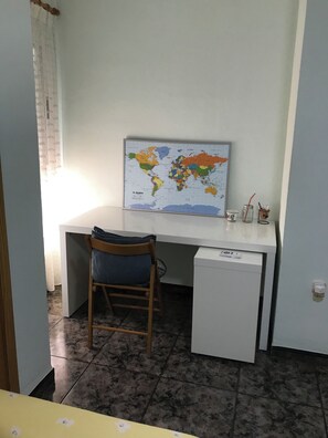 Ein kleines Zimmer mit Schreibtisch, Stuhl und einer Karte an der Wand.