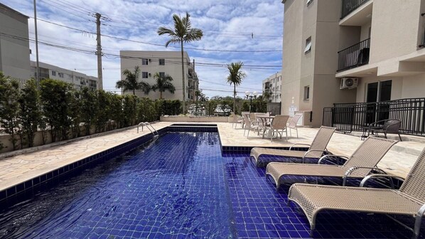 Ein Pool mit Liegestühlen, umgeben von Gebäuden und Palmen.