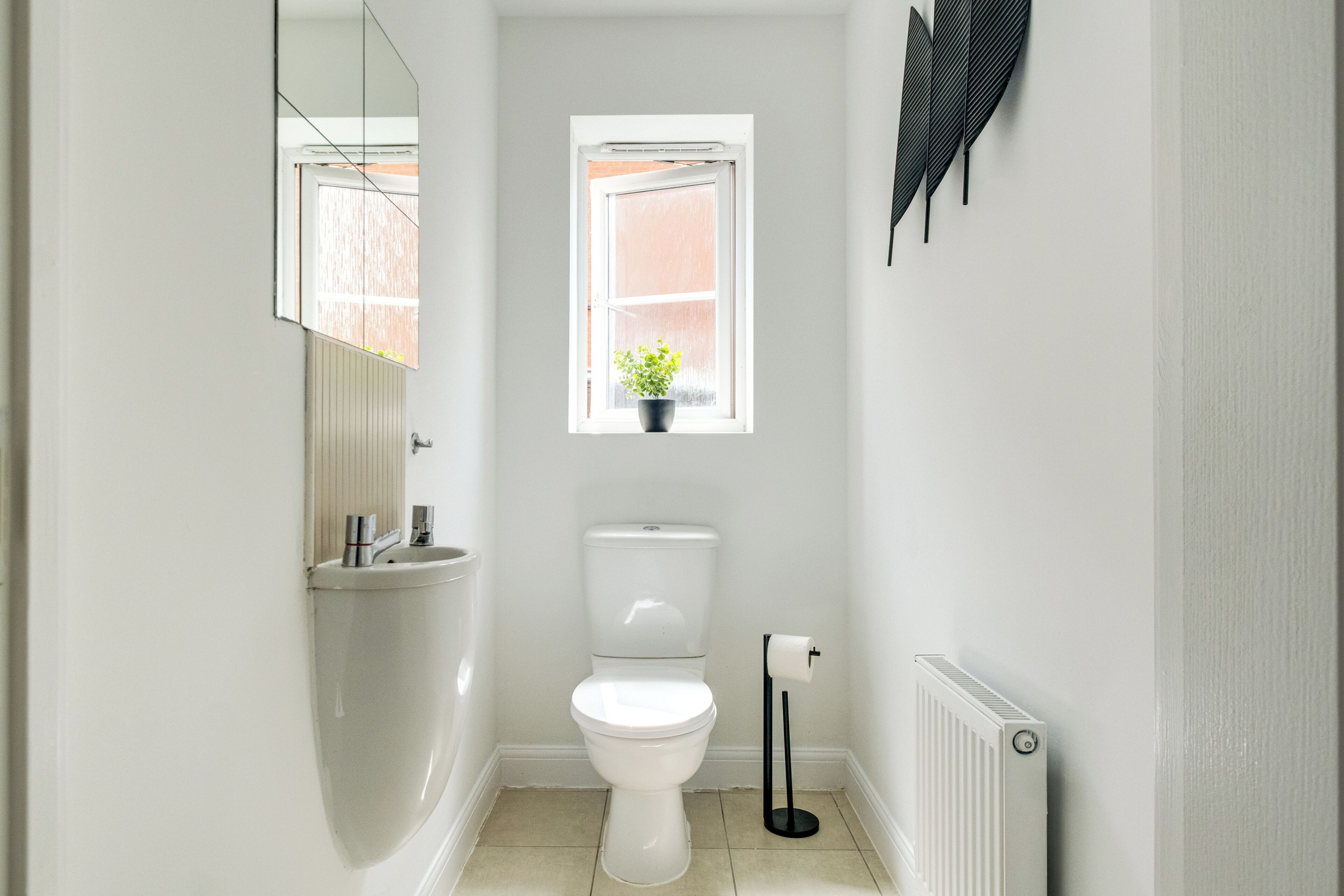 A small, white bathroom with a toilet, a sink, a window with a plant, and a radiator.