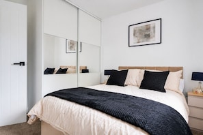 A bedroom with a bed, bedside tables, a wardrobe, a mirror, and a framed picture on the wall. - Modern 4BR House Perfect for long stays｜Free Parking and Wifi (Walsall)
