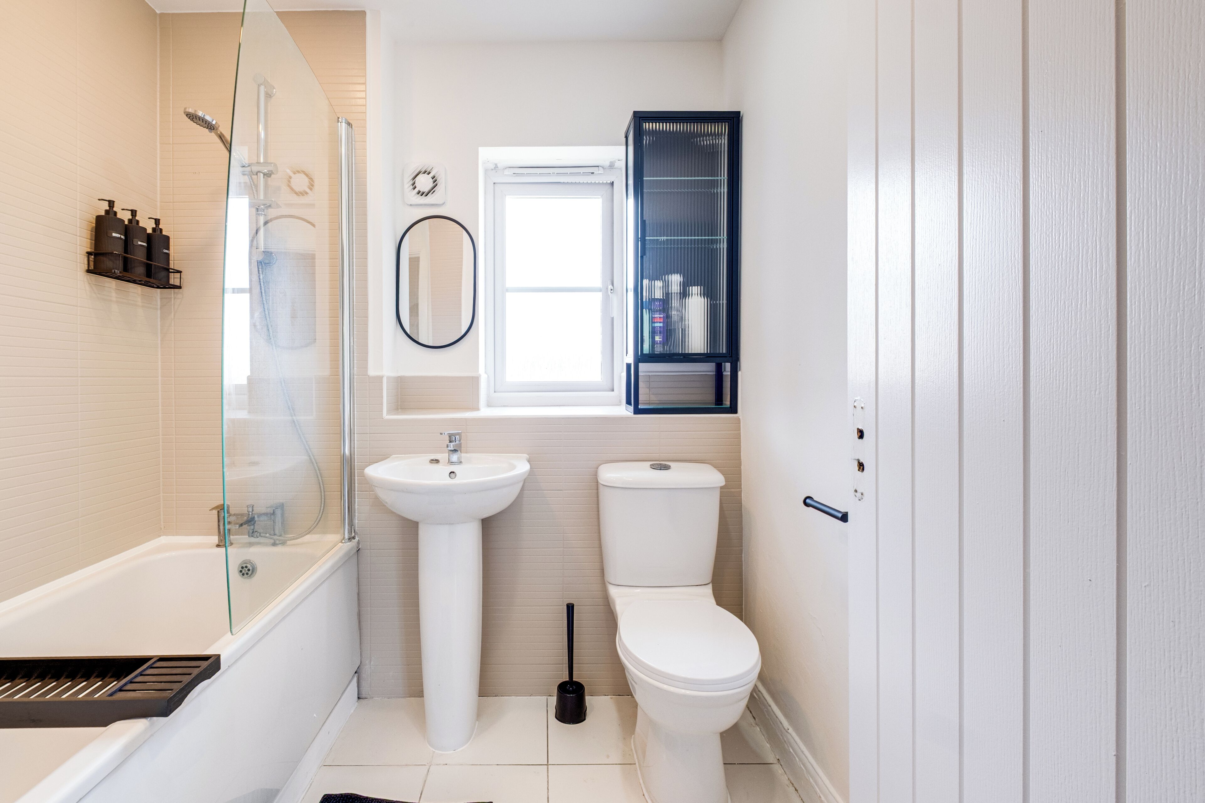 A modern bathroom with a glass-enclosed shower, a pedestal sink, a toilet, and a medicine cabinet.
