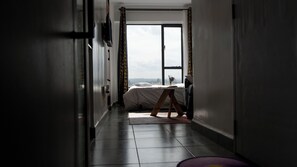 Ein Flur, der zu einem Schlafzimmer führt, mit einem Bett, einem Fenster und einem an der Wand befestigten Fernseher.