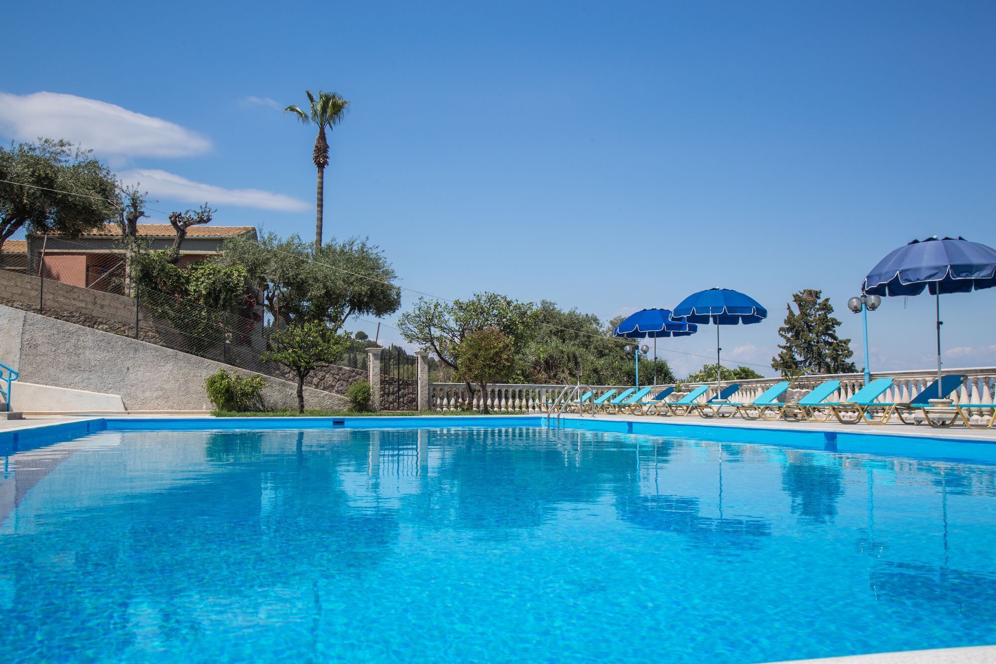 A swimming pool with clear blue water, surrounded by lounge chairs and blue umbrellas.