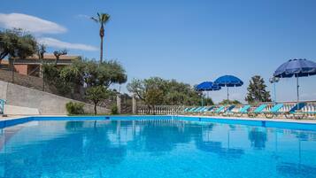 A swimming pool with clear blue water, surrounded by lounge chairs and blue umbrellas.