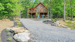 A log cabin with a balcony, surrounded by a gravel driveway and a forested area. - Deep Creek Mountain Retreat (McHenry)