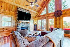 A log cabin interior with a stone fireplace, wooden ceiling, and large windows. - Deep Creek Mountain Retreat (McHenry)