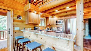 A wooden cabin interior with a kitchen, bar area, and bar stools. - Deep Creek Mountain Retreat (McHenry)