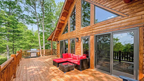 A wooden deck with a red sofa and a grill, surrounded by glass doors and windows. - Deep Creek Mountain Retreat (McHenry)