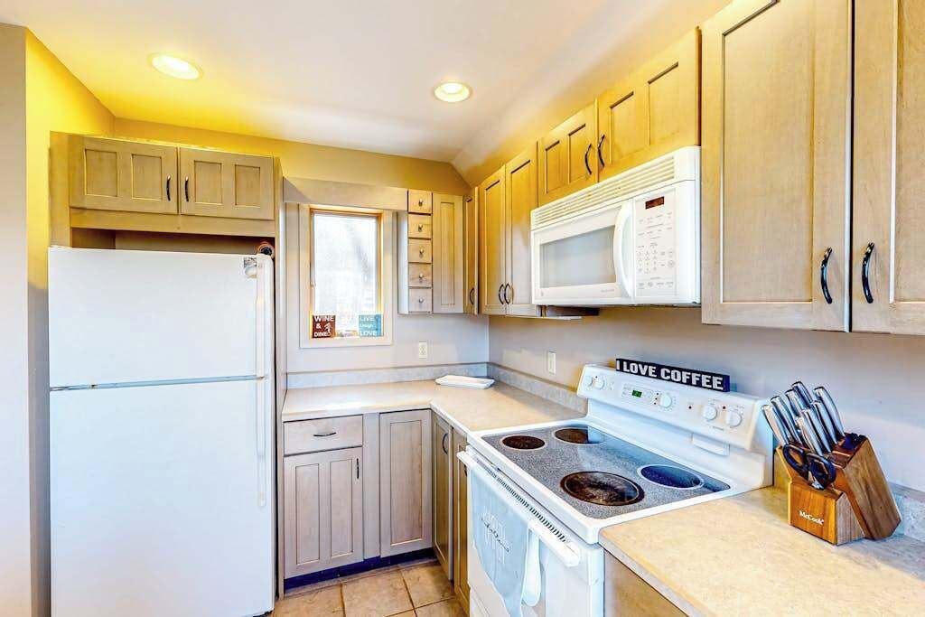 A compact kitchen with a refrigerator, microwave, stove, and wooden cabinets.