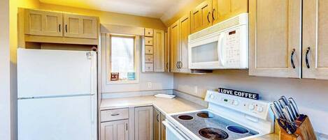A compact kitchen with a refrigerator, microwave, stove, and wooden cabinets.