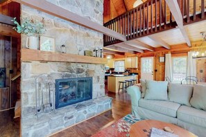 A stone fireplace, wooden beams, a kitchen, and a living area with a sofa and coffee table.