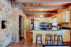 A kitchen with wooden beams, a stone wall, and a central island with stools.