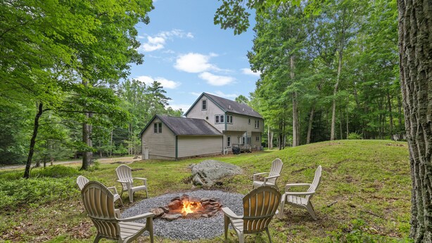 A house with a fire pit and Adirondack chairs in a wooded area. - Poconos Family Retreat | 5 Acres | Sleeps 15 (Barrett Township)