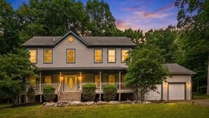 A two-story house with a porch, a garage, and a well-maintained lawn. - Poconos Family Retreat | 5 Acres | Sleeps 15 (Barrett Township)