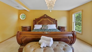 A bedroom with a large bed, a chandelier, a window with a view, and a small round table. - Poconos Family Retreat | 5 Acres | Sleeps 15 (Barrett Township)