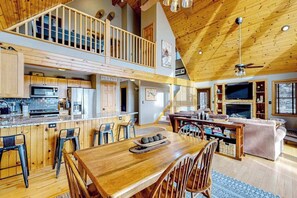 Eine geräumige Küche mit Essbereich, ein Wohnzimmer mit Kamin und ein Schlafzimmer im oberen Bereich mit Balkon.