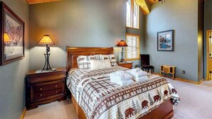 A bedroom with a wooden ceiling, a bed with a patterned bedspread, two bedside lamps, a nightstand, and a framed picture on the wall. - 5BR - Chalet - Hot Tub (McHenry)