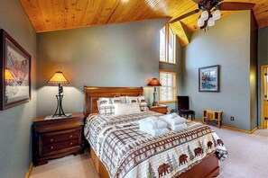 Ein Schlafzimmer mit Holzboden, einem Bett mit gemustertem Überwurf, zwei Nachttischlampen, einem Nachttisch und einem gerahmten Bild an der Wand.