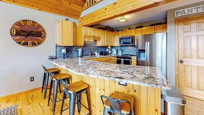 A kitchen with wooden cabinets, a granite countertop, and a bar stool area. - 5BR - Chalet - Hot Tub (McHenry)