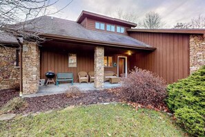 A house with a stone exterior, a covered porch with wicker furniture, and a stone pillar. - Charming 4BR Lodge - HOT TUB - Swanton (Swanton)