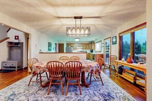 A dining area with a table and chairs, a kitchen in the background, and a large window. - Charming 4BR Lodge - HOT TUB - Swanton (Swanton)
