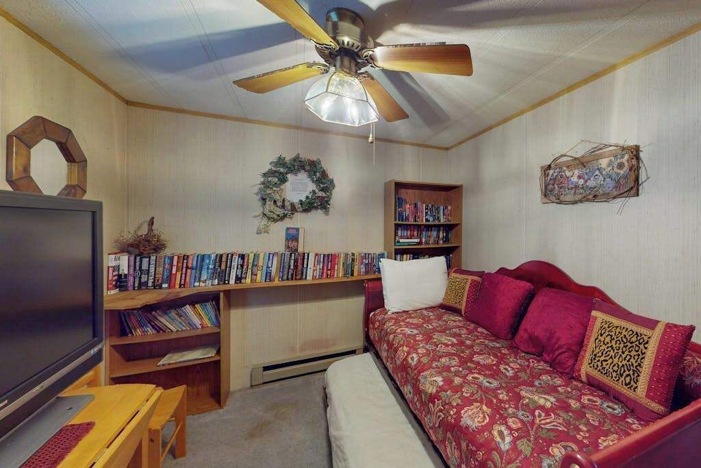 Una habitación con ventilador de techo, televisor, estantería, sofá y un adorno decorativo en la pared.