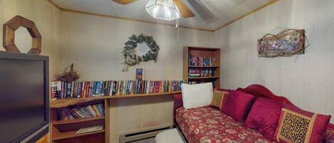 A room with a ceiling fan, a television, a bookshelf, a couch, and a decorative wreath on the wall.