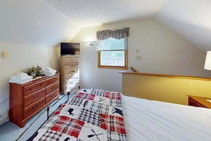 Ein Schlafzimmer mit Bett, Kommode, Fernseher und einem Fenster mit Jalousien.