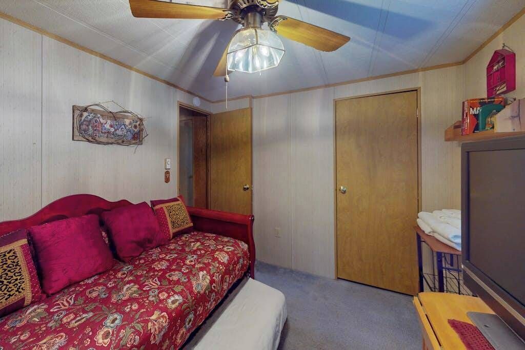 A bedroom with a bed, a ceiling fan, a wardrobe, a television, and a desk with a keyboard.