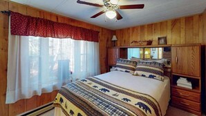 A bedroom with a bed, wooden walls, a ceiling fan, and a window with curtains. - 3BR - Cozy Cabin - Hot Tub (McHenry)