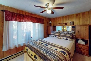 A bedroom with a bed, wooden walls, a ceiling fan, and a window with curtains. - 4BR - Cozy Cabin - Hot Tub (McHenry)