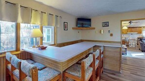 A kitchen with a dining area, wooden benches, a TV, and a window with curtains. - 3BR - Cozy Cabin - Hot Tub (McHenry)