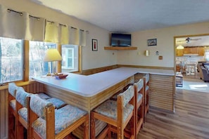 A kitchen with a dining area, wooden benches, a TV, and a window with curtains. - 4BR - Cozy Cabin - Hot Tub (McHenry)