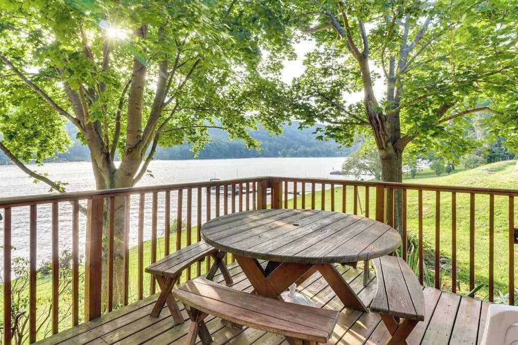 Een houten terras met een ronde tafel en bankjes, met uitzicht op een meer.