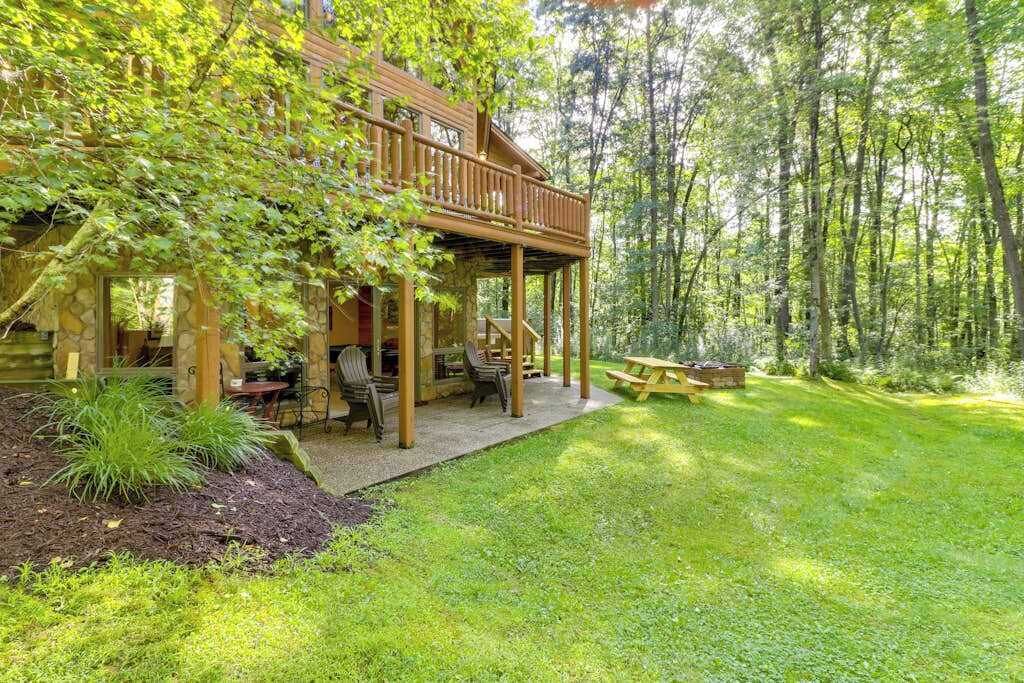 Eine Holzhütte mit überdachter Veranda, umgeben von einem üppigen Rasen und dichtem Wald.